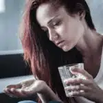 A woman holds a glass of water in one hand and pills in the other - 5 Warning Signs Of Xanax Addiction
