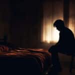 A man sits on a stool in a dimly lit bedroom - Dexedrine Side Effects, Interactions, & Warnings