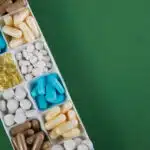 Pills and capsules of multiple shapes and colors are in a white tray on a green background - Identifying Ritalin Pills What Does Ritalin Look Like