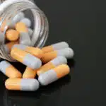 Orange and while capsules spill out of a glass bottle - Is Ritalin (Methylphenidate) Addictive