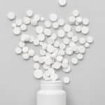 A pile of round, white pills pouring out of a white bottle - Ritalin (Methylphenidate) Side Effects In Adults | Short-Term & Long-Term Effects
