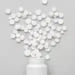 A pile of round, white pills pouring out of a white bottle - Ritalin (Methylphenidate) Side Effects In Adults | Short-Term & Long-Term Effects