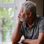 A senior man sits alone at a table looking out a window - Vyvanse & Depression How To Manage Vyvanse Crash Symptoms