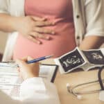 a preganant woman sits at a doctor's desk while the doctor writes on a clipboard - Vyvanse Use During Pregnancy | Safety & Risks