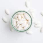 A glass jar containing white pills, more pills are scattered around the jar - How Long Does Concerta Stay In Your System
