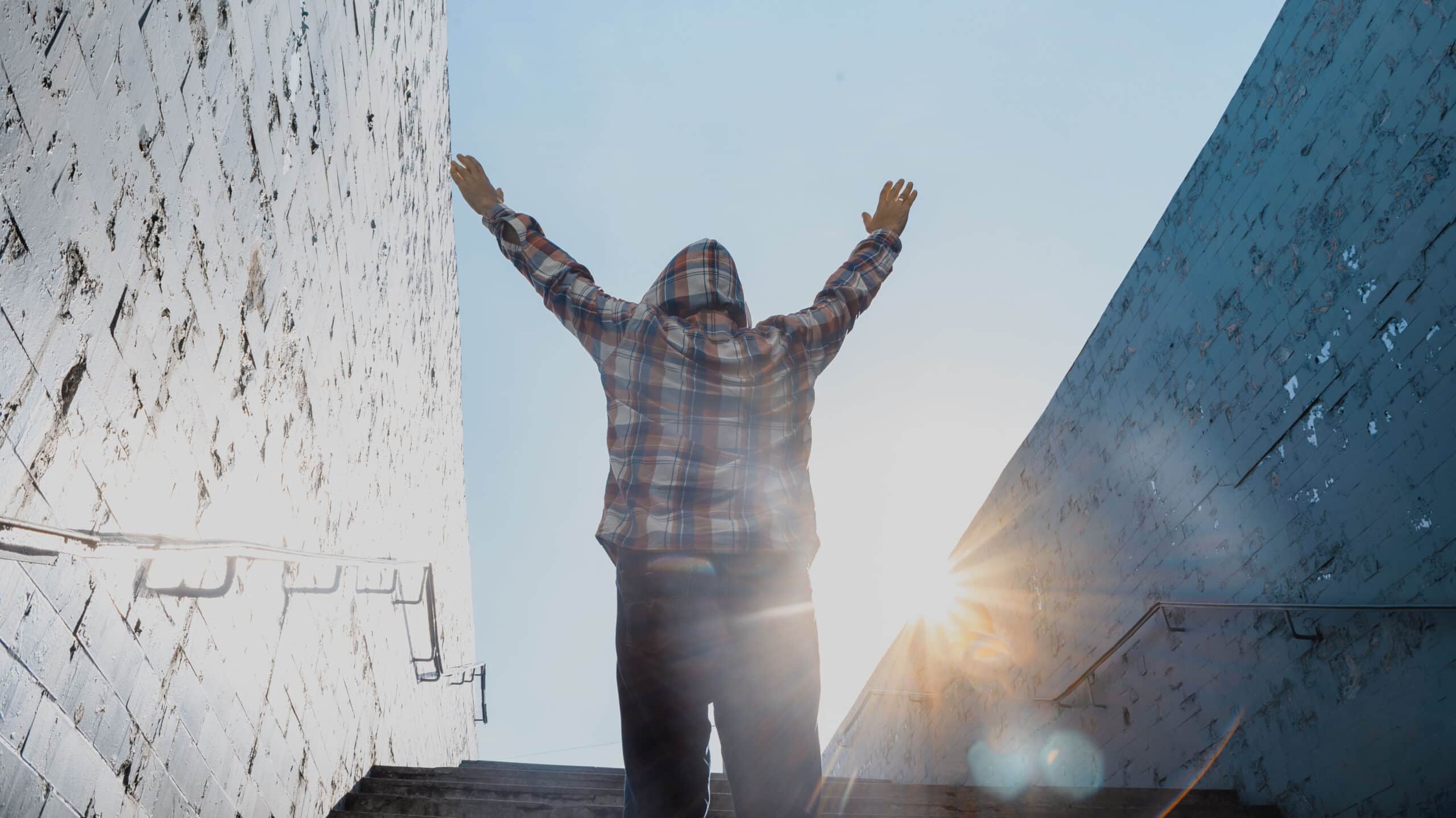 A man triumphantly walks up stairs holding his hands to the sky - How To Rebuild Your Life & Find Purpose After Addiction