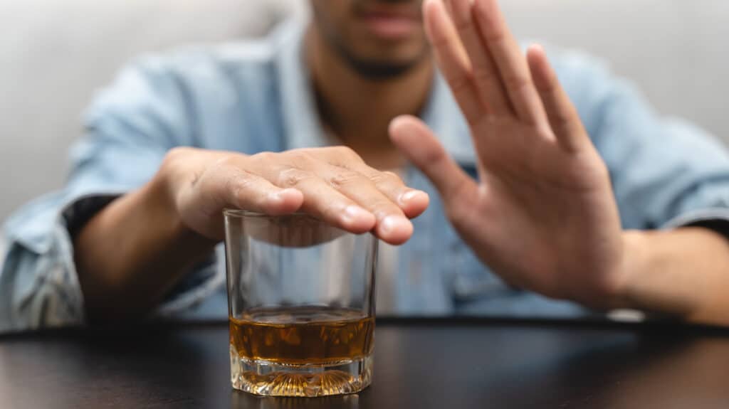 A man covers a liquor glass with his right hand and holds up his left hand - Is It Okay To Drink Alcohol In Addiction Recovery