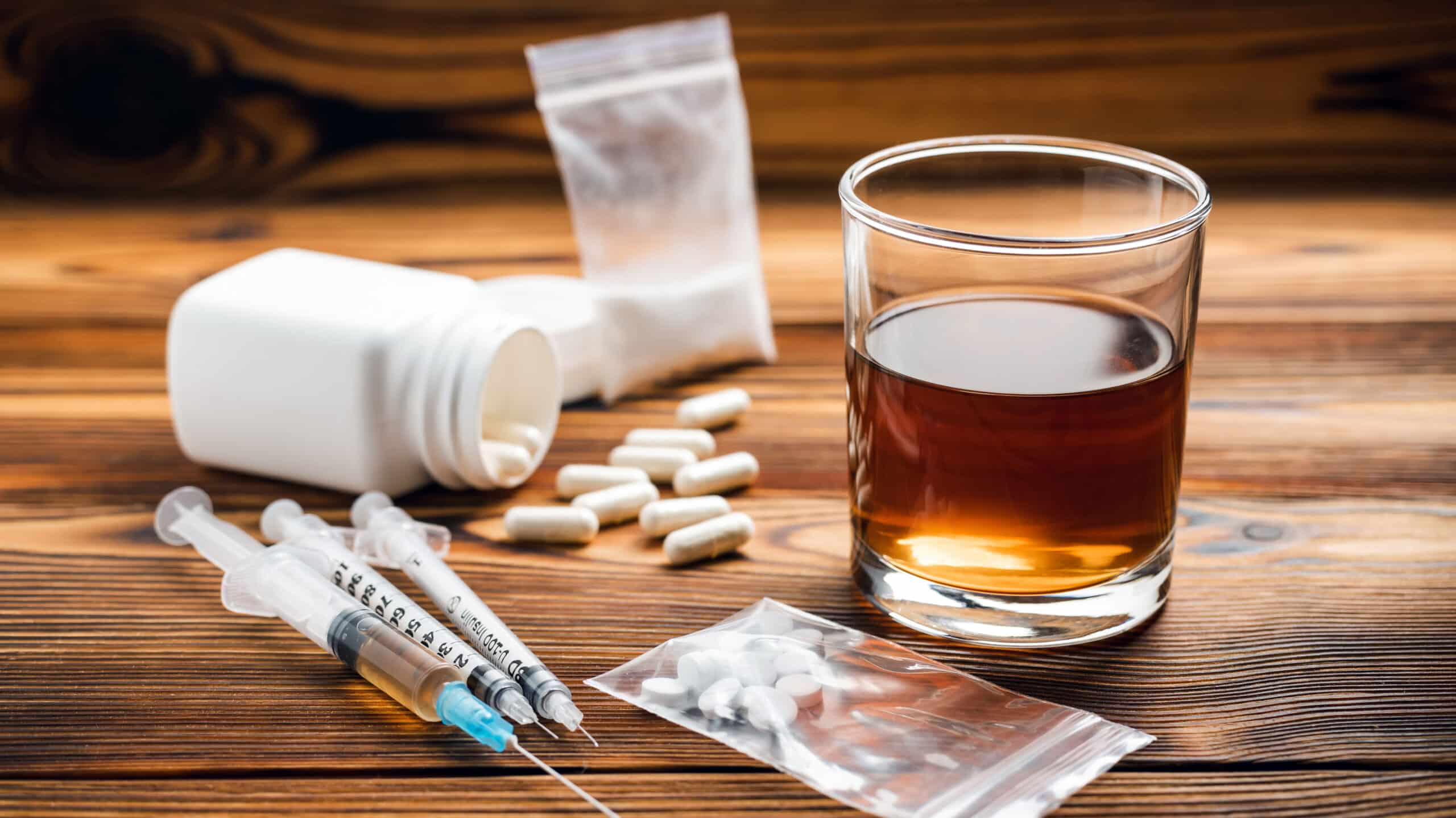 A glass of alcohol surrounded by pills, a syringe, and powders - Myths and Facts About Drug Abuse & Addiction